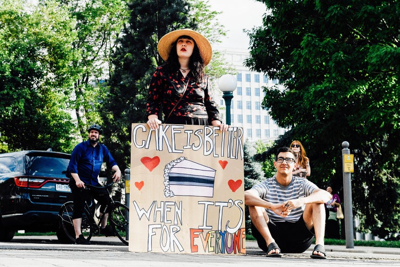 Woman holding a sign that says, "Cake is better when it's for everyone."